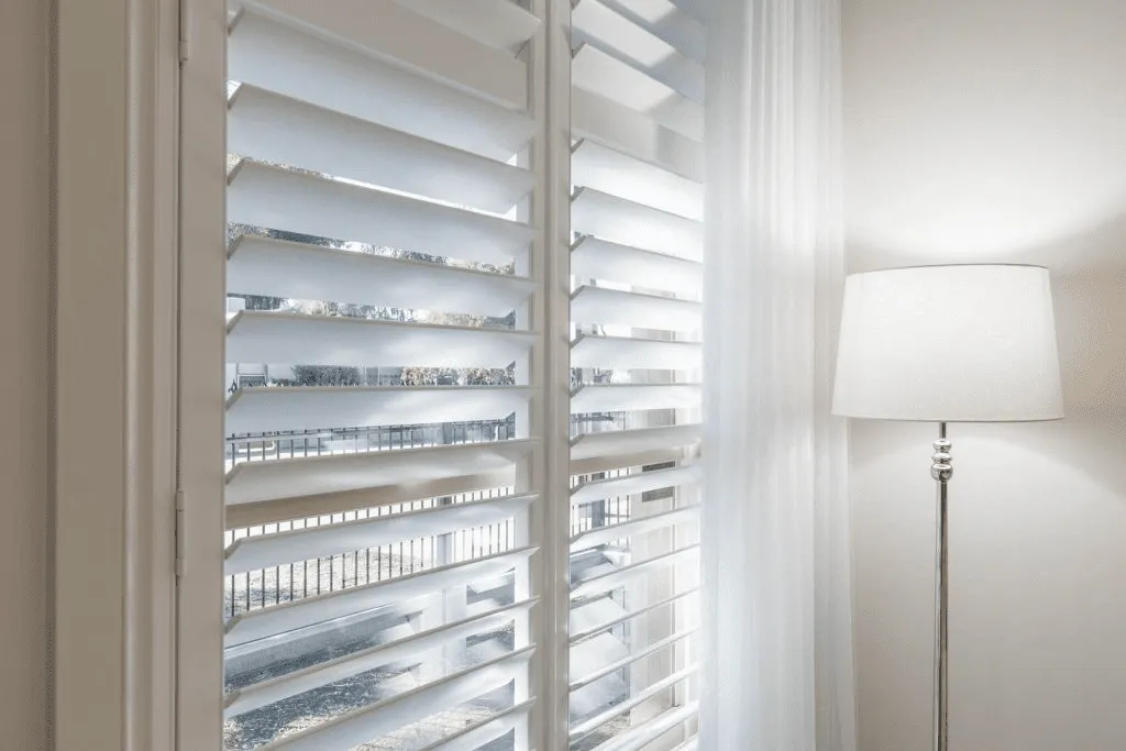 White plantation shutters and lamp showcasing custom window treatments