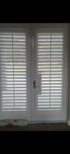White plantation shutters covering double doors with an outdoor view.