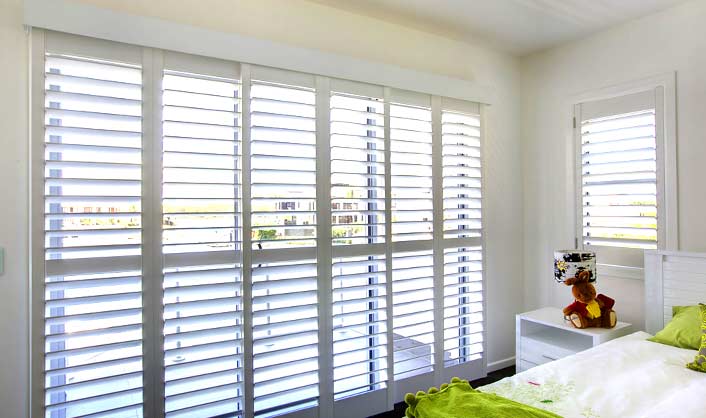 Custom plantation shutters in a bright bedroom, showcasing Liberty Shutters’ durable window treatments.